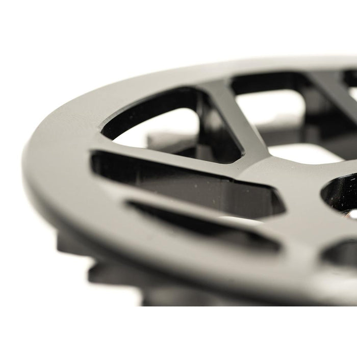 Close-up of a black Colony Bish Guard Sprocket, featuring triangular openings and beveled edges. CNC machined from aluminum, it showcases a lightweight design resembling a gear or mechanical part.