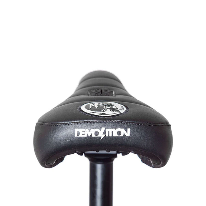 The Demolition Matt Cordova Seat (V1) is a black BMX seat with a white "DEMOLITION" logo on the back, showcasing the Pivotal Fat Cap design. It’s attached to a seat post against a plain background, highlighting Matt Cordova's impact on its style and functionality.