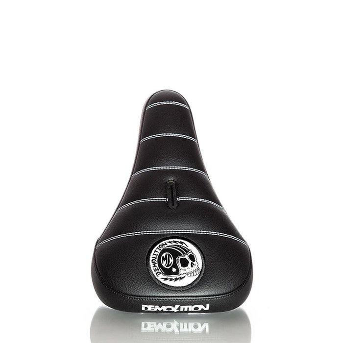 The Demolition Matt Cordova Seat (V2) is a black bicycle seat featuring a skull design, made from durable leatherette materials. It includes the word "Demolition" printed on it and offers Pivotal Fat Cap Padding for improved comfort during your rides.