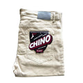 A pair of beige chino pants folded neatly, with a label on the back pocket that reads "Double Stretch Premium Chino, FP MFG." These FP Pants Relaxed Fit Chino Bone are designed with skate enthusiasts in mind.