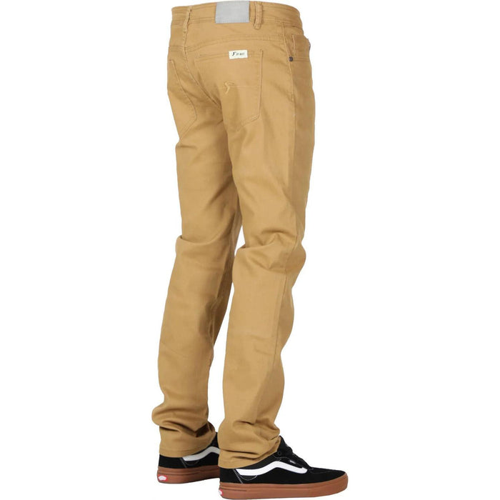 A person is standing, wearing khaki **FP Pants Relaxed Fit Chino Bone** and black sneakers with white accents. The pants, made of stretch fabric, have a small white label near the back pocket. The background is white.