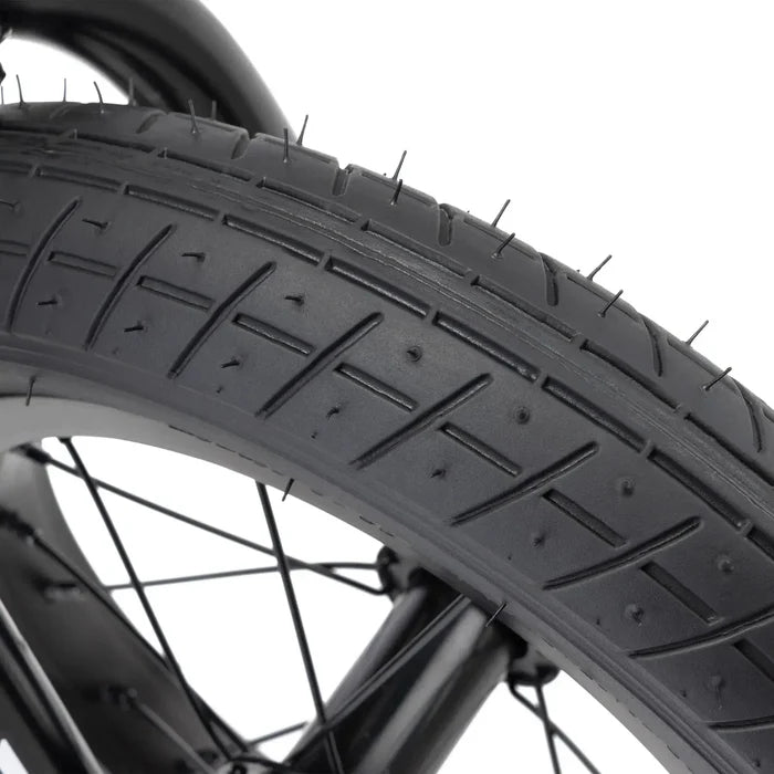 Close-up of a black tire with tread and rubber nubs, plus black spokes—showcasing the Kink Roaster 12 Inch Bike (2026), ideal for kids or anyone picking their first BMX bike.