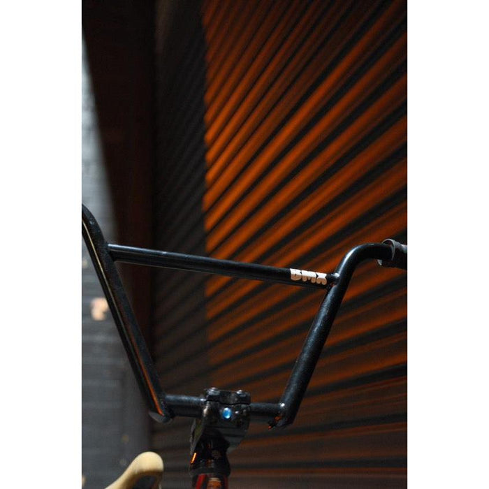 Close-up of the Kink Williams 4-Piece Bars, made from durable chromoly tubing, set against a corrugated metal wall and bathed in warm light.