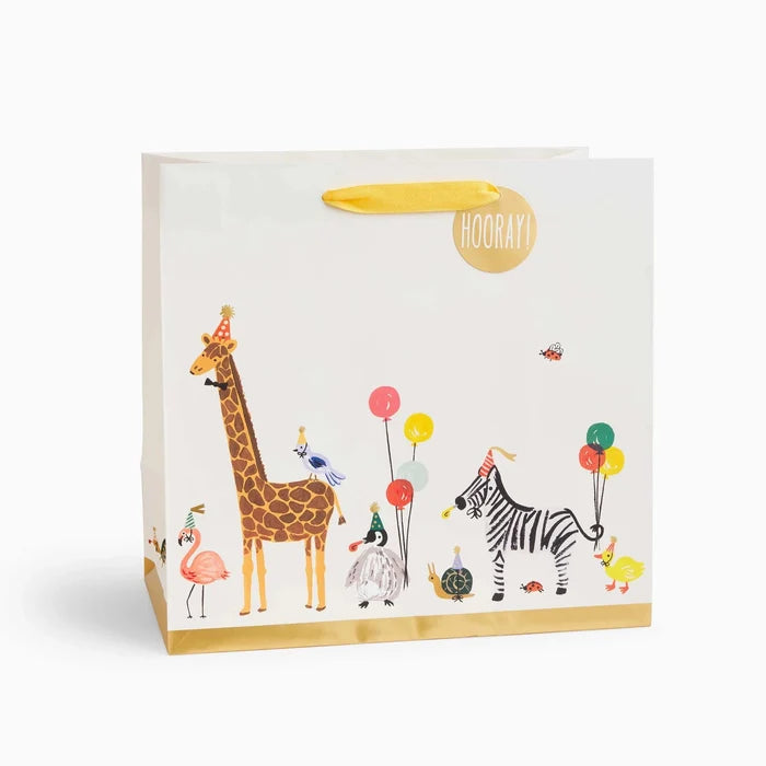 A large gift bag with a parade of animal characters including a giraffe, zebra, and others, decorated with metallic gold foil accents and cotton ribbon handles.