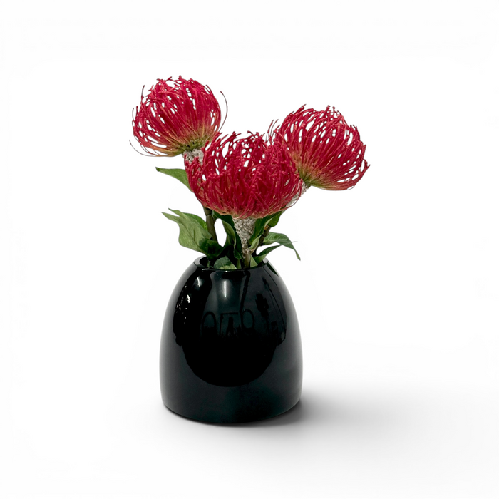 Black vase with red faux pincishion flowers on a white background