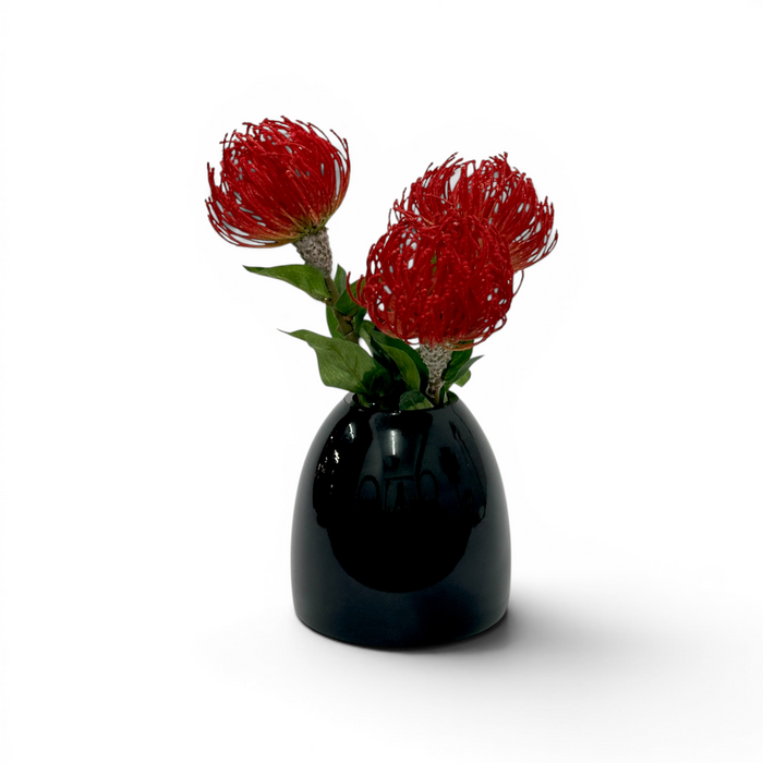 Black vase with red fake pincusion flowers on a white background