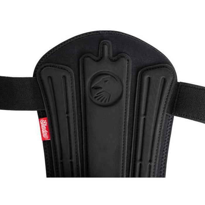 Close-up of the Shadow Invisa-Lite Shin/Ankle Pad Combo (Youth) (Pair) in black with two straps, raised animal emblem, and 3D impact foam for enhanced protection. Red tag with white "Shadow" text highlights its sturdy design—ideal for young athletes.