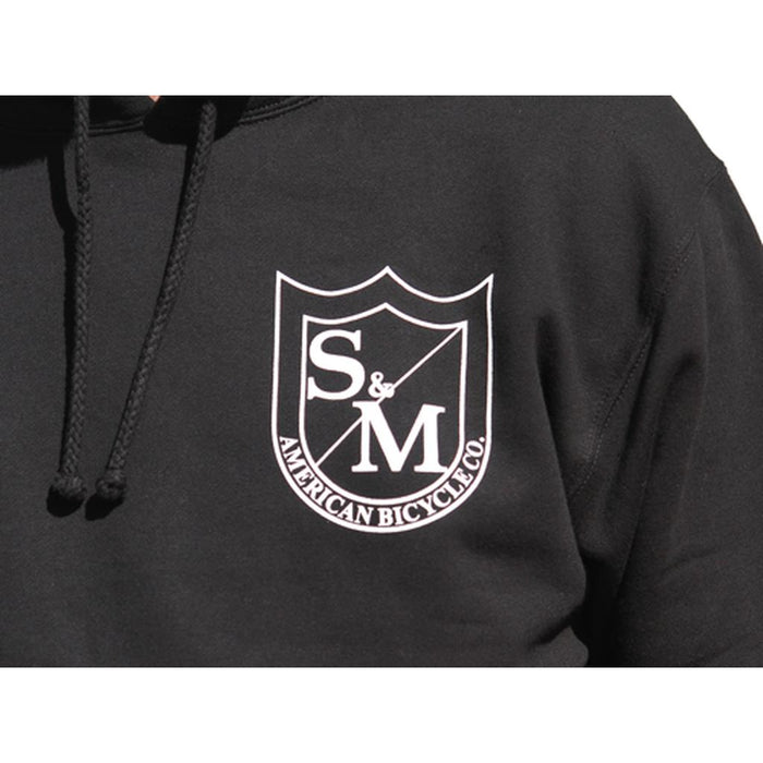 The S&M Two Shield Pullover Hoodie features a white shield logo with "S & M American Bicycle Co." on the chest, a cozy fleece-lined hood, and is crafted for comfort—sweet hoods, printed in the USA.