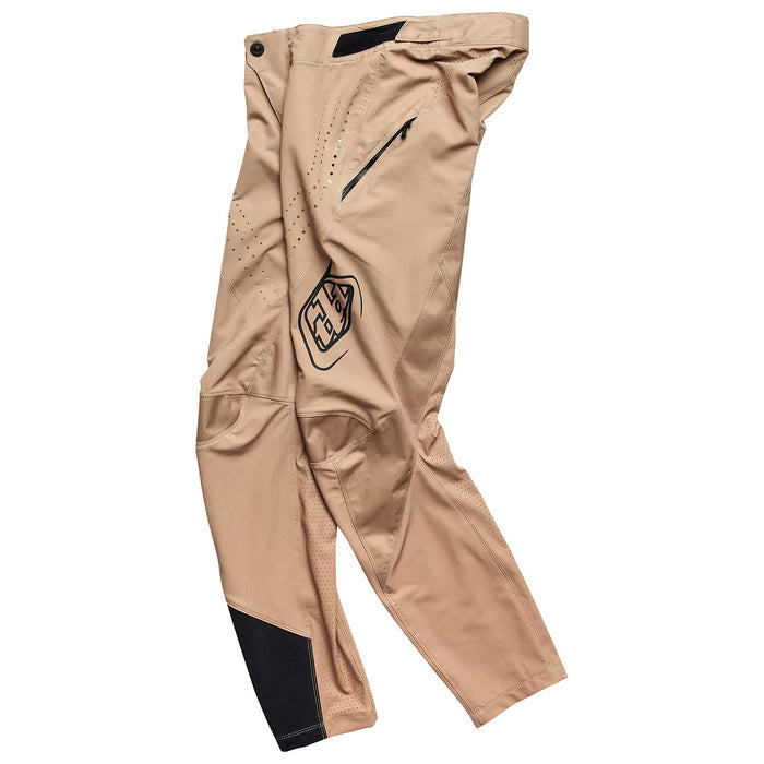 The TLD Sprint Pant Mono Oak athletic pants, designed for BMX racing, feature a tan color with a black logo, black reinforced knee patch, side zipper pocket, and ventilation holes—displayed against a white background.